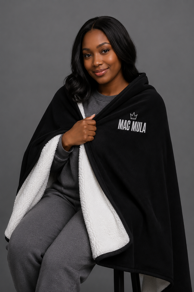 Woman wrapped in the MAC MULA Embroidered Sherpa Blanket, showing the plush white sherpa reverse
